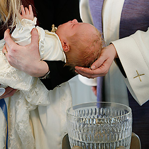 Ett barn som hålls över dopfunt i glas och prästen döper.